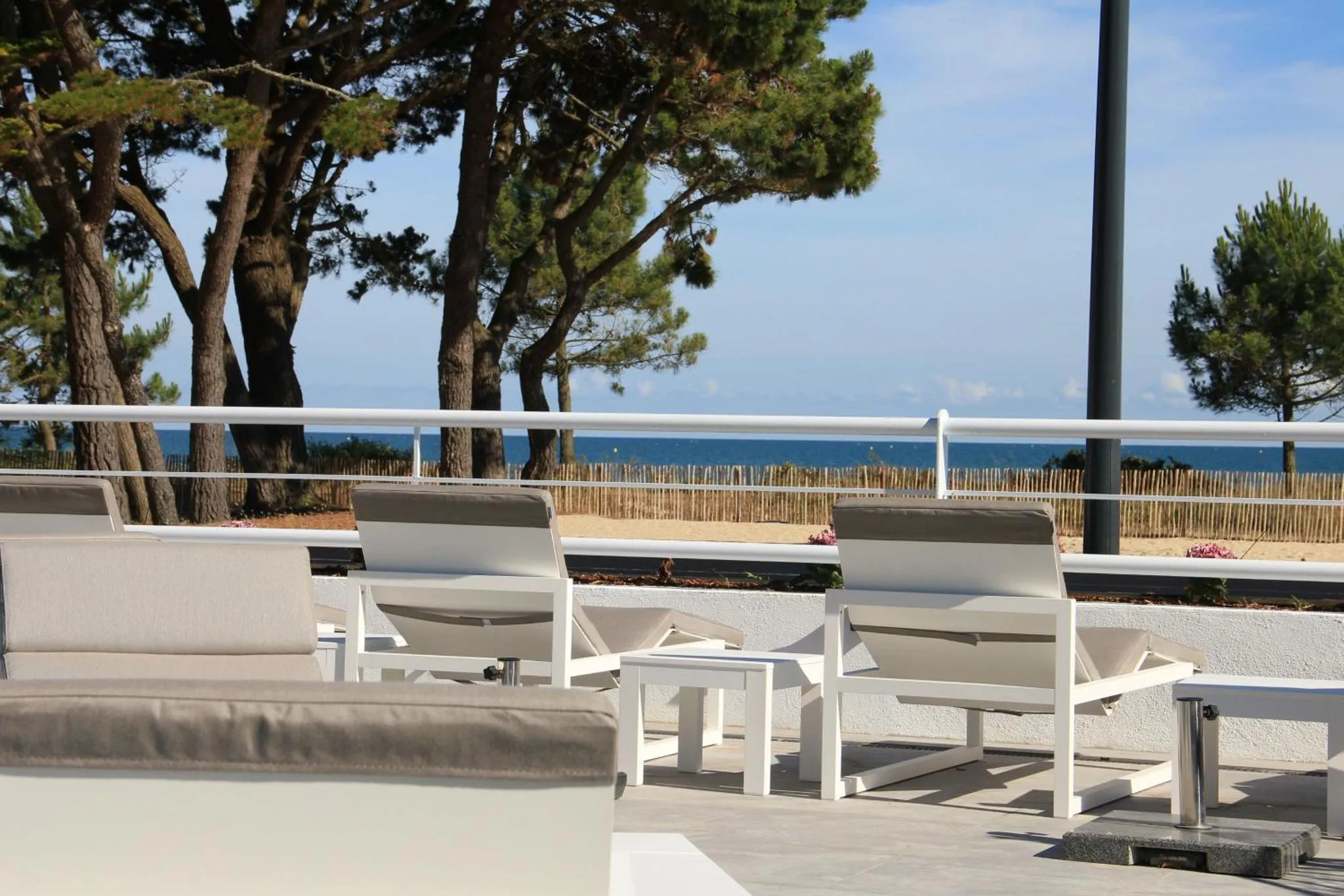 Transats blancs sur une terrasse ensoleillée avec vue sur la mer.