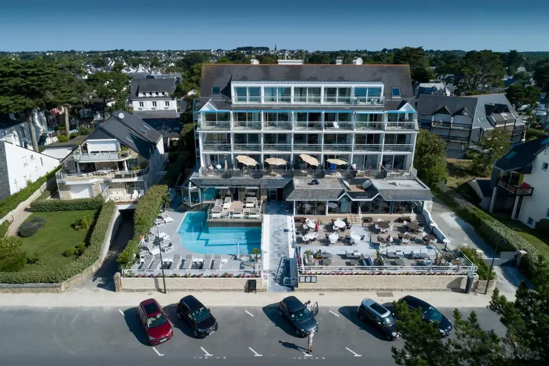 Vue aérienne d'un bâtiment blanc avec des terrasses et une piscine en bord de mer.