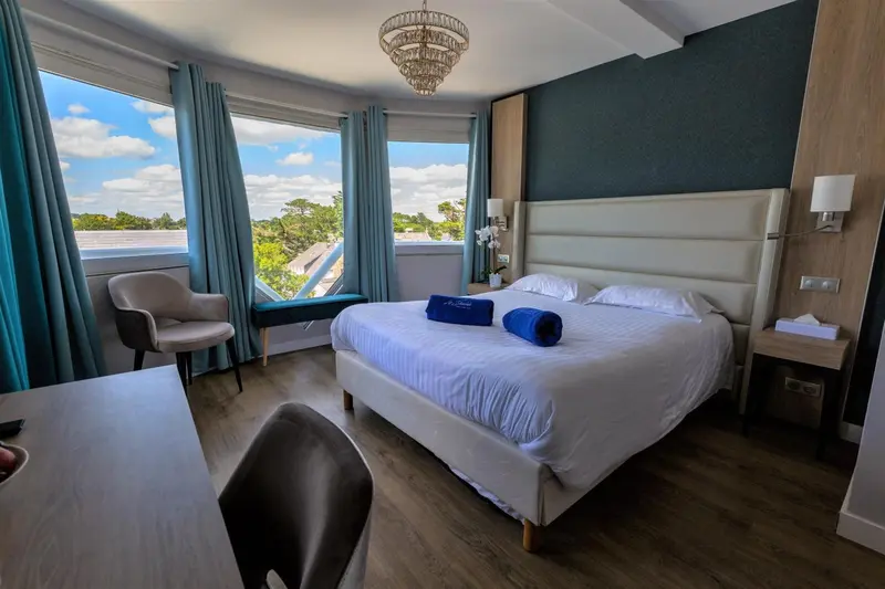 Chambre lumineuse avec un grand lit et une vue sur la végétation.