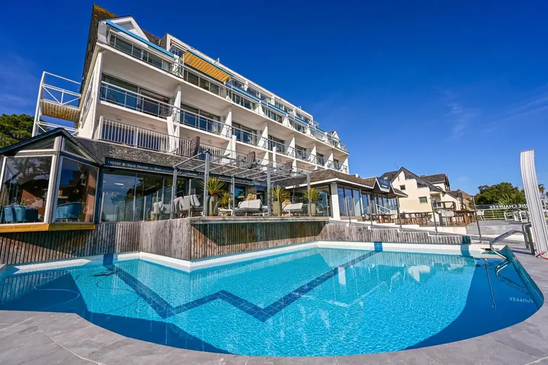 Bâtiment blanc avec balcons et piscine bleue au premier plan.