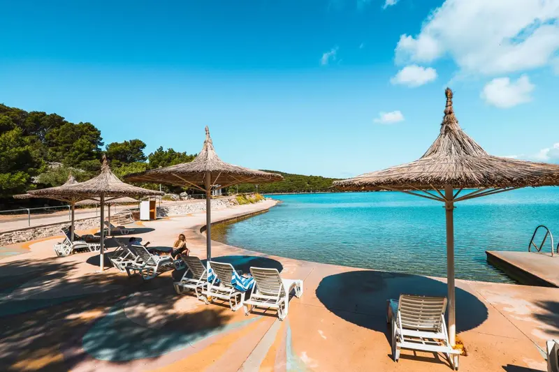 Transats et parasols de paille sur une terrasse ensoleillée au bord de l'eau.