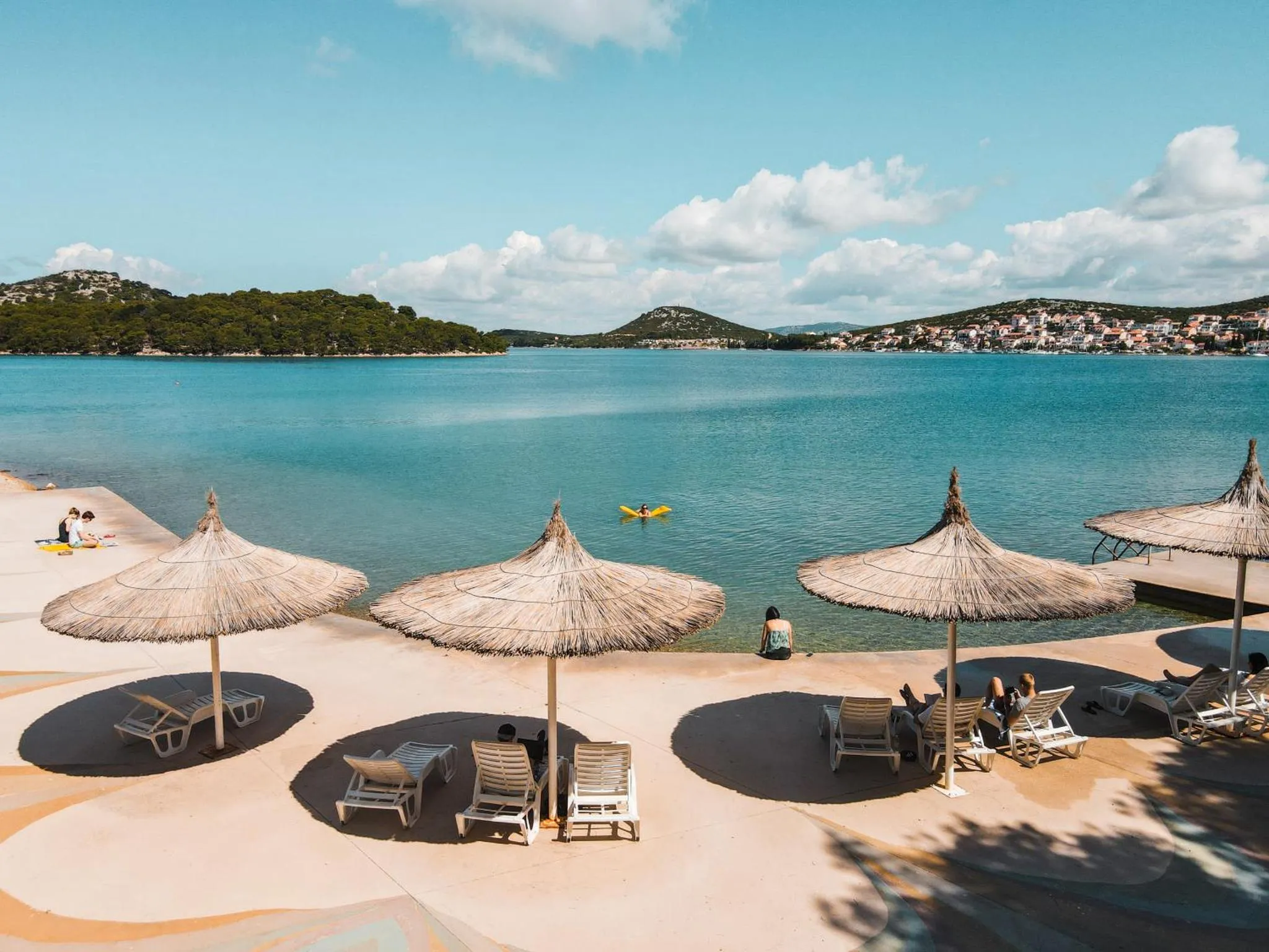 Plage de sable avec parasols de chaume et transats en bord de mer.