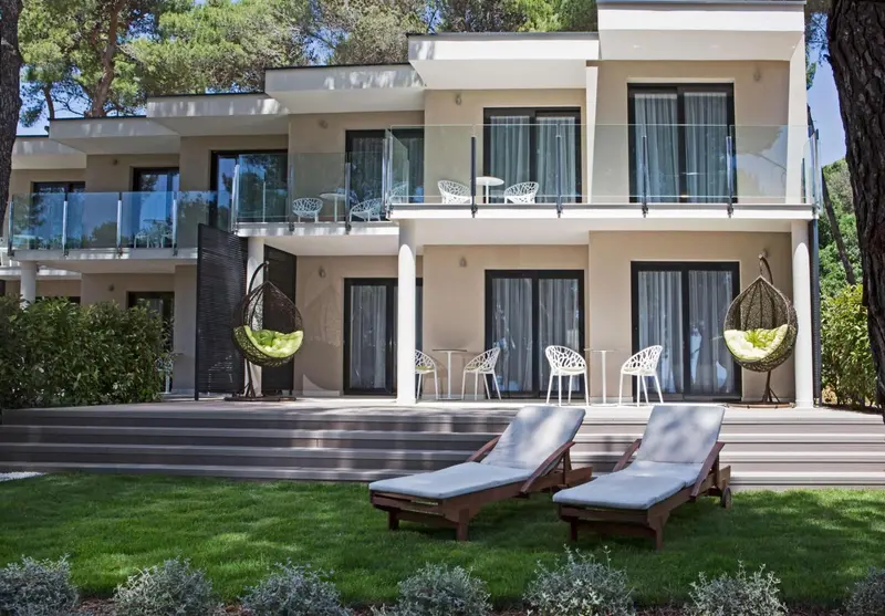 Façade d'un bâtiment moderne avec des transats et des fauteuils suspendus sur une pelouse.