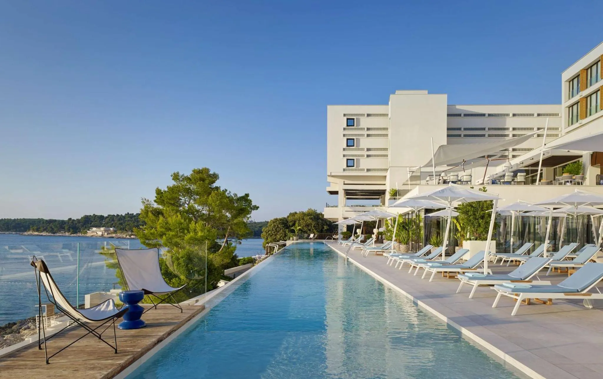 Une longue piscine bordée de transats blancs offre une vue sur la mer.