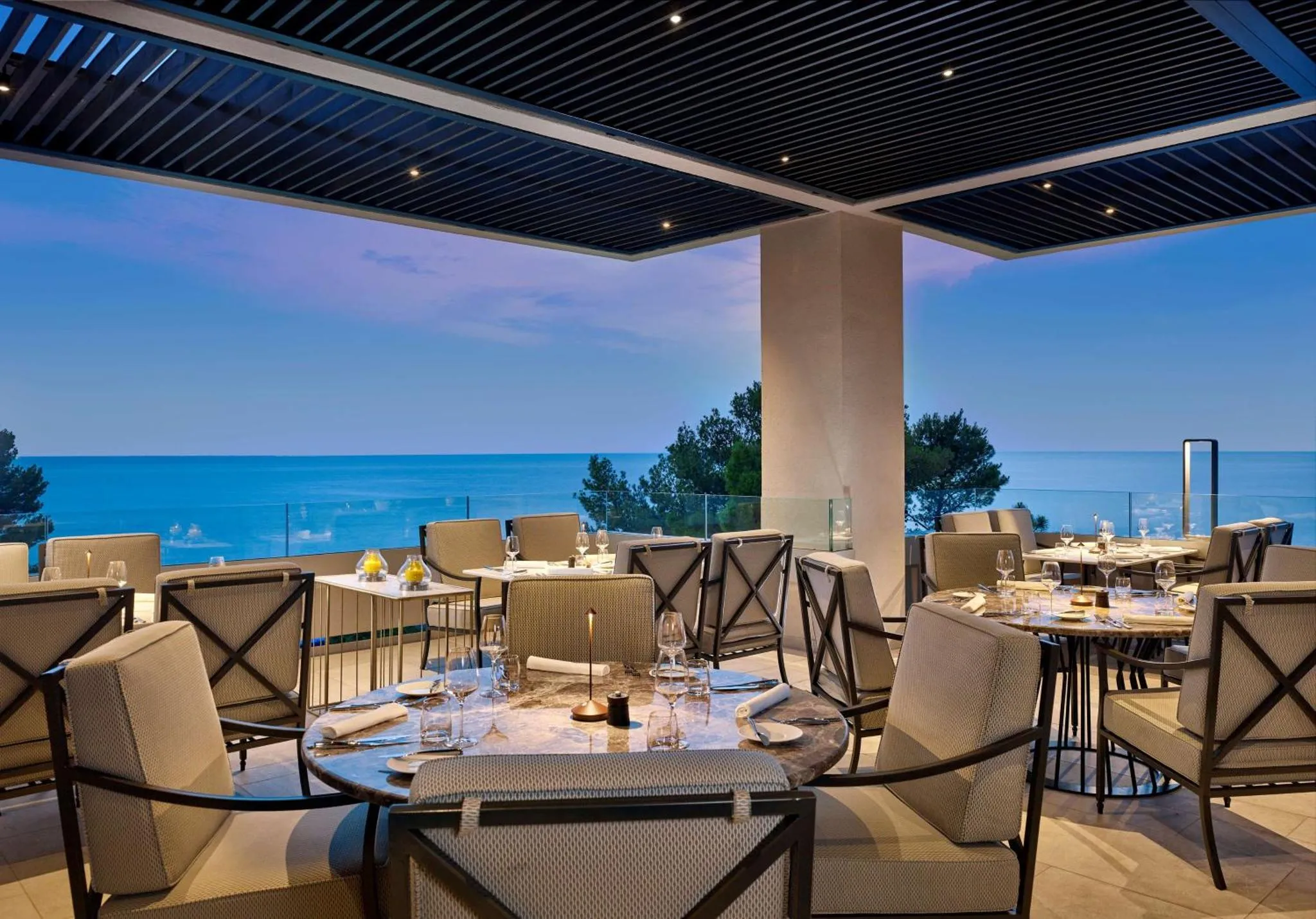 Tables dressées en terrasse avec vue sur la mer au crépuscule.
