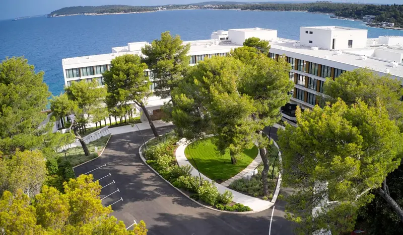 Vue aérienne d'un bâtiment blanc moderne entouré de végétation et surplombant la mer.