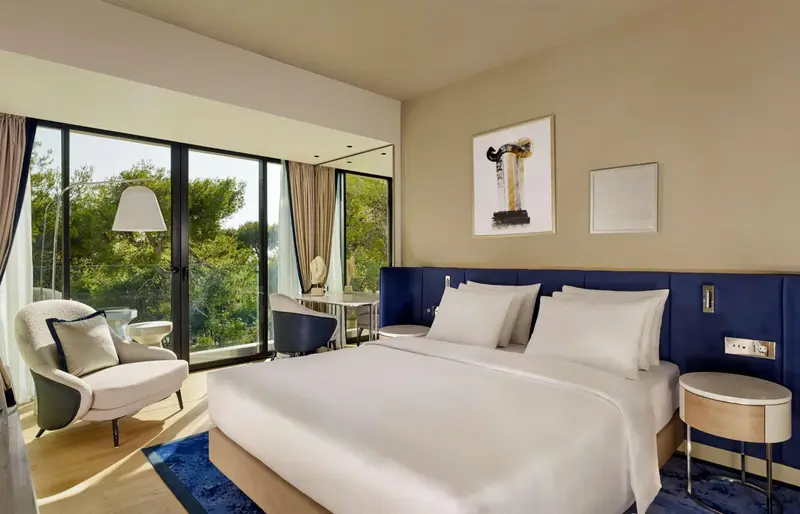 Une chambre lumineuse avec un grand lit et un coin salon près d'une baie vitrée.