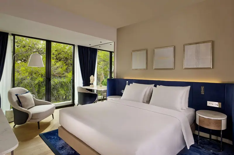 Chambre lumineuse avec un grand lit et un fauteuil près d'une fenêtre.