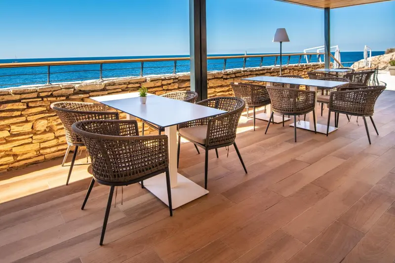 Terrasse avec tables et chaises donnant sur la mer.