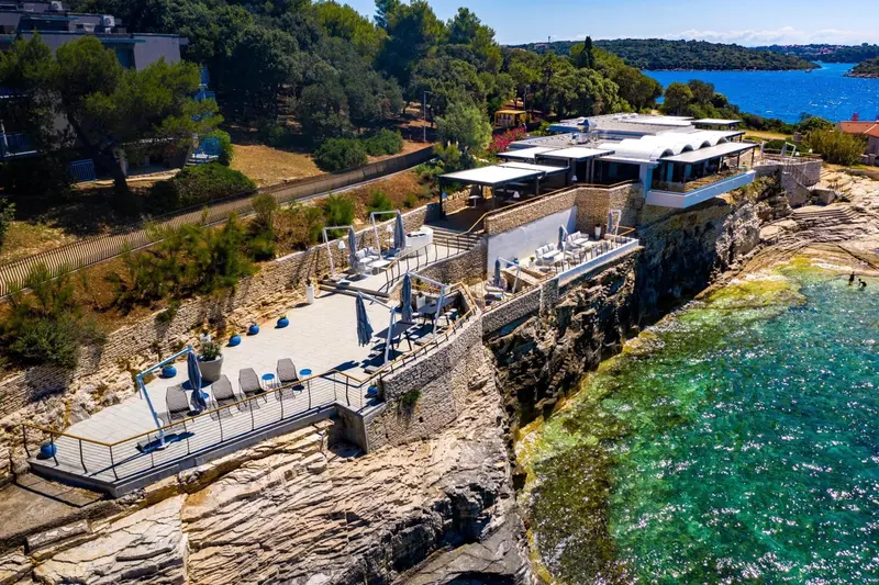 Terrasse aménagée avec transats et parasols surplombant une côte rocheuse et la mer.