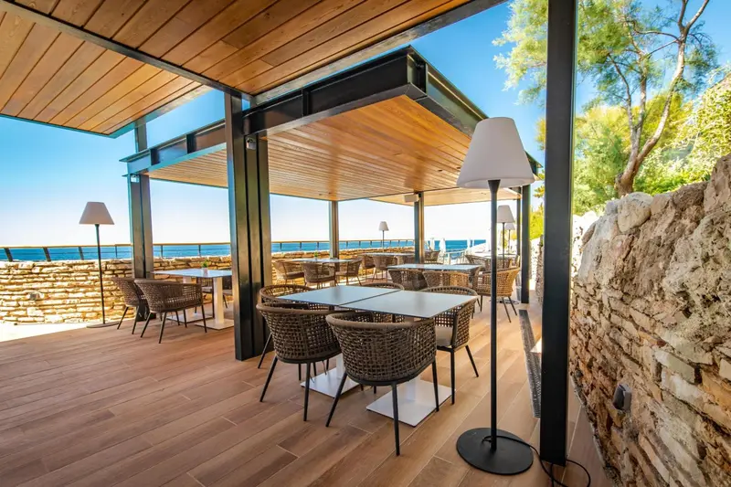 Terrasse ombragée avec tables et chaises en osier donnant sur la mer.