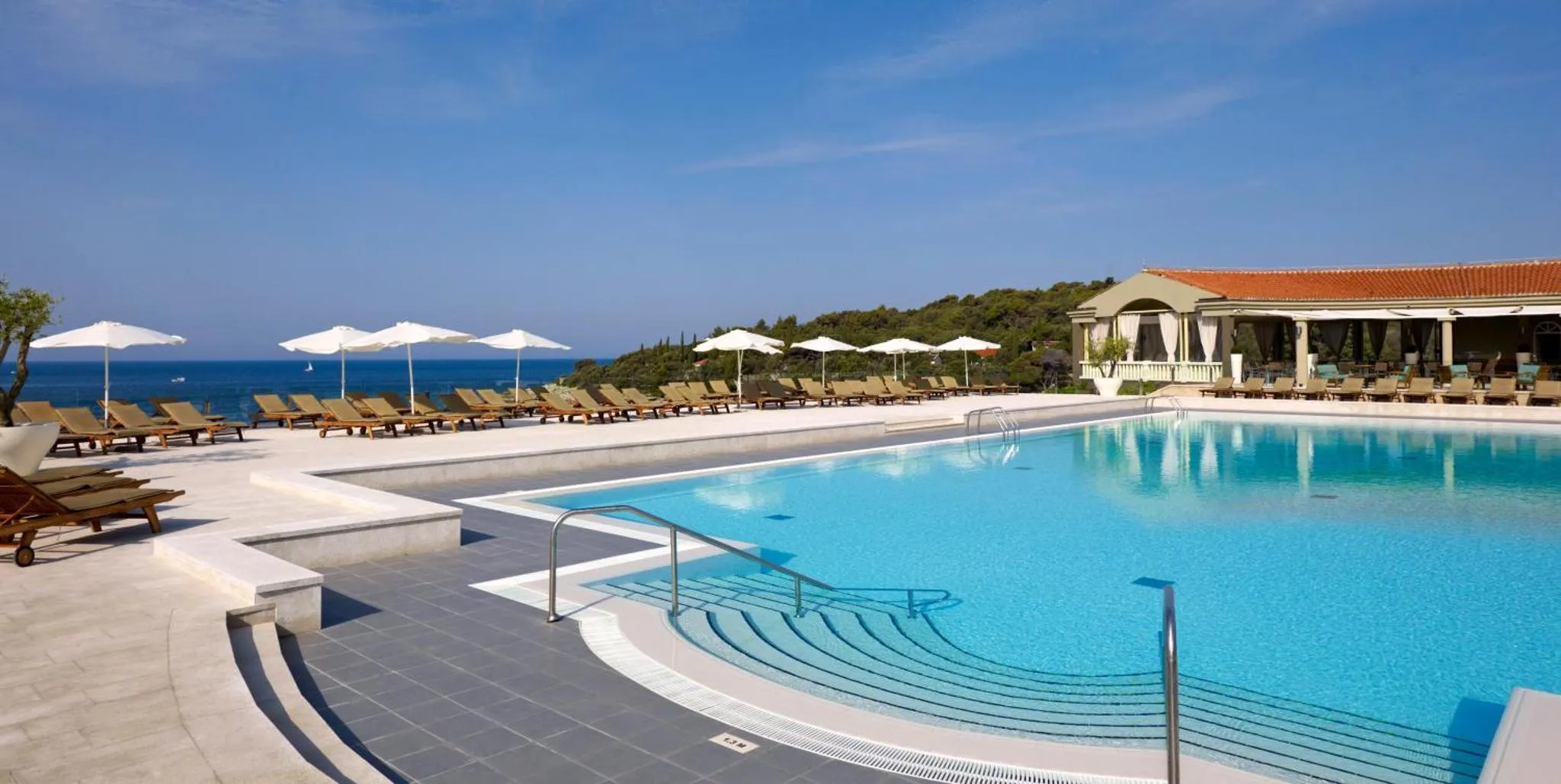 Une piscine bleue bordée de transats blancs, avec une vue sur la mer.