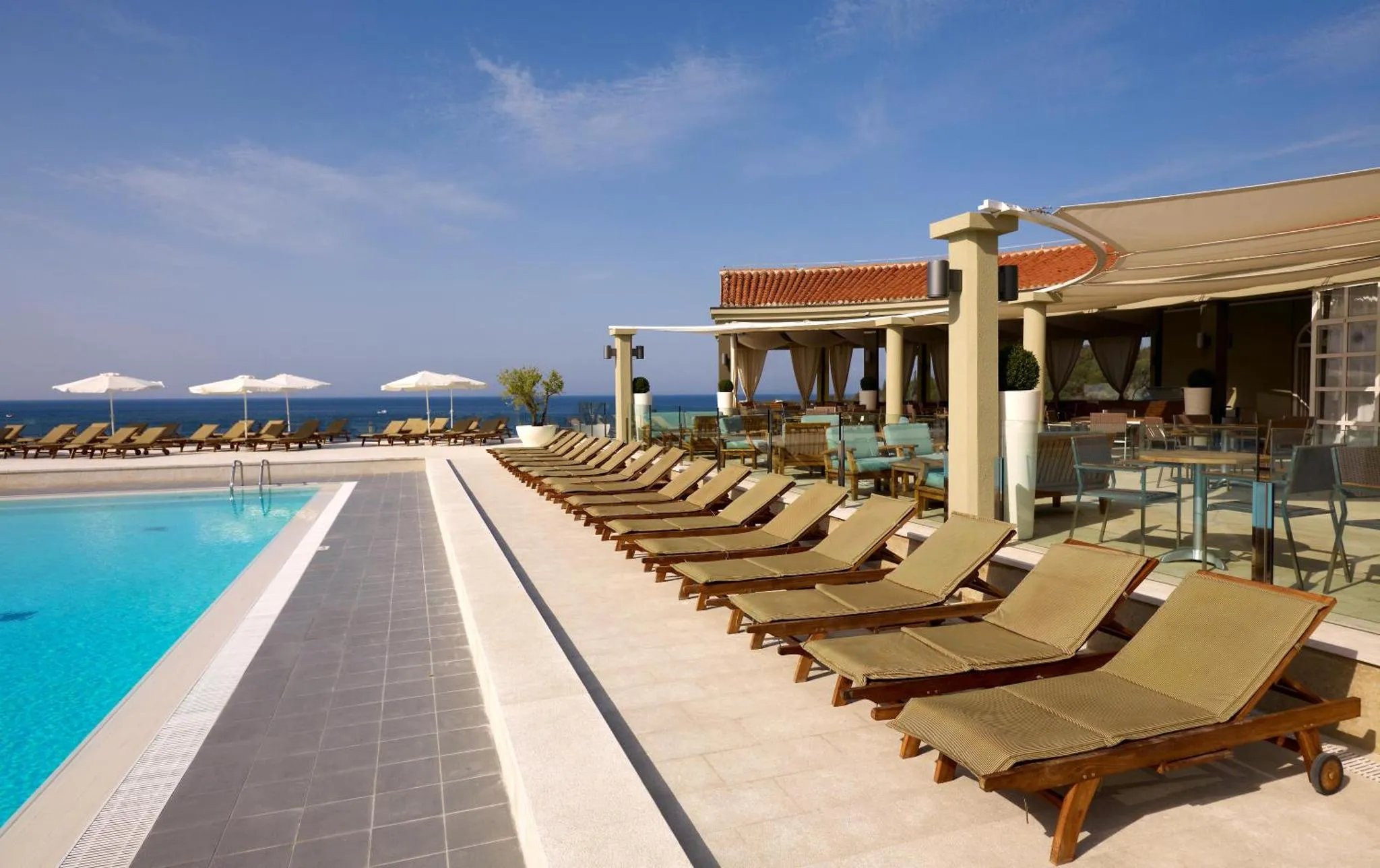 Transats alignés au bord d'une piscine ensoleillée avec vue sur la mer.
