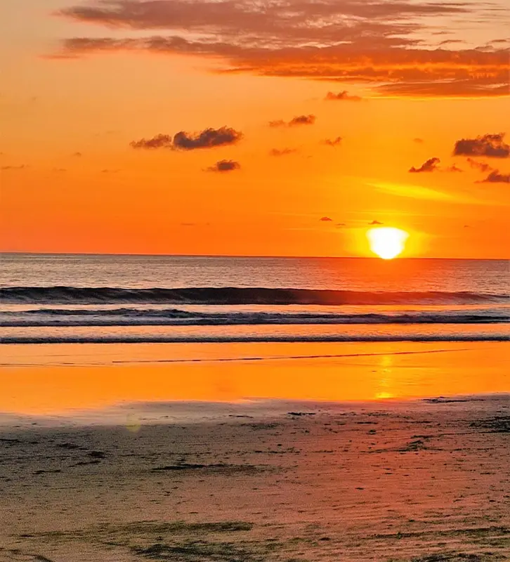 Le soleil se couche sur une plage de sable fin, illuminant la mer d'une lumière orangée.