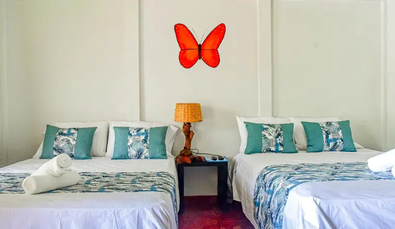 Deux lits jumeaux décorés de coussins turquoise dans une chambre lumineuse.
