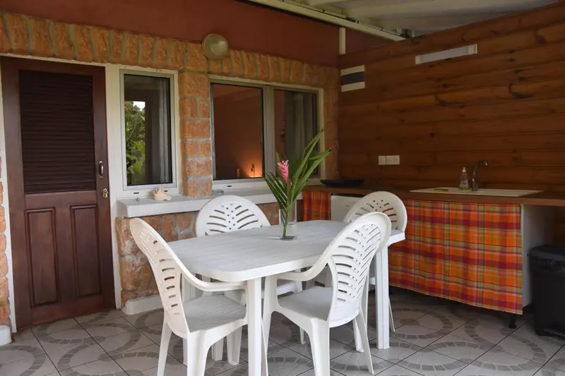 Une table et des chaises blanches sont disposées devant une cuisine extérieure.