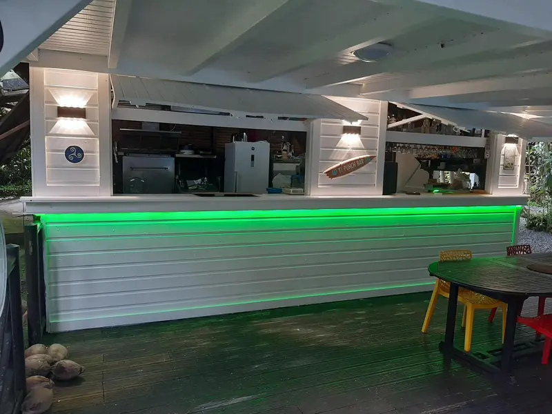 Un bar extérieur illuminé de couleur verte avec des tabourets et des tables.