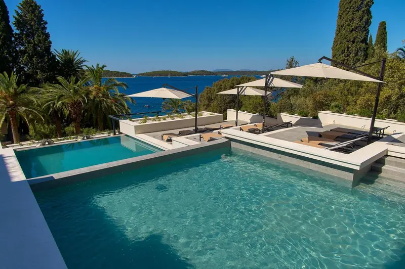 Une piscine rectangulaire bordée de transats et de parasols offre une vue sur la mer.