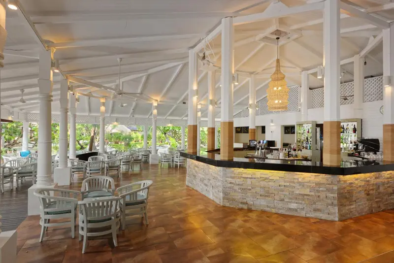 Un bar lumineux avec un comptoir incurvé en pierre et des tables disposées en extérieur.