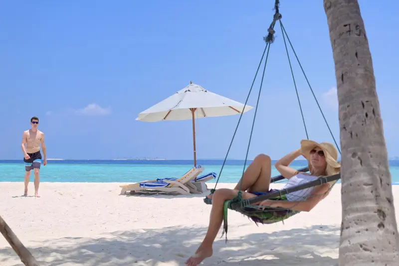 Une femme se détend dans un hamac sur une plage de sable blanc.
