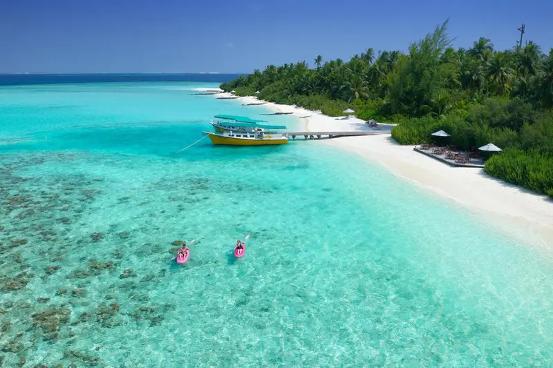 Vue aérienne d'une plage de sable blanc bordée d'une eau turquoise et d'une végétation luxuriante.