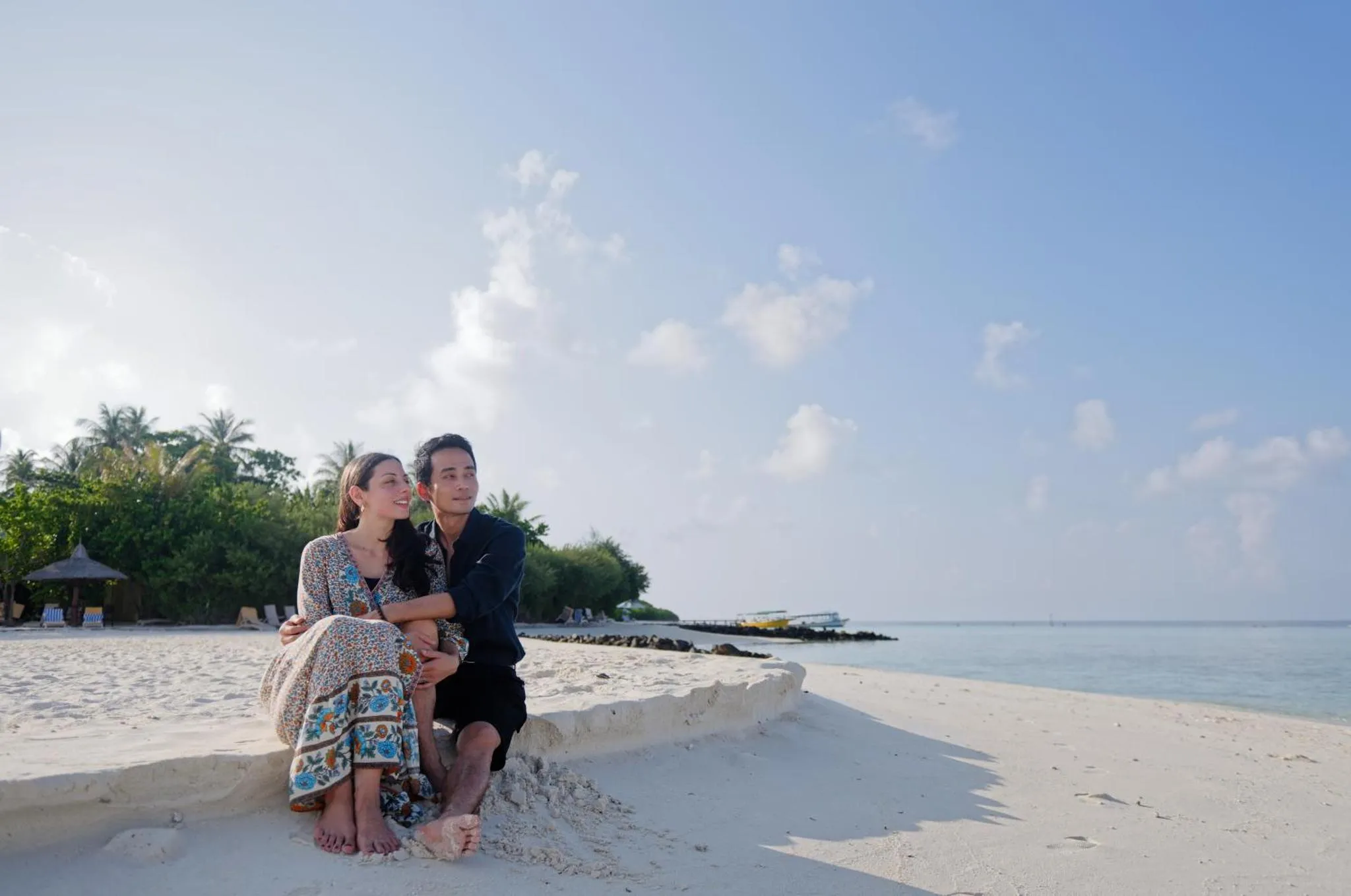 Un couple se tient sur une plage de sable blanc face à la mer.
