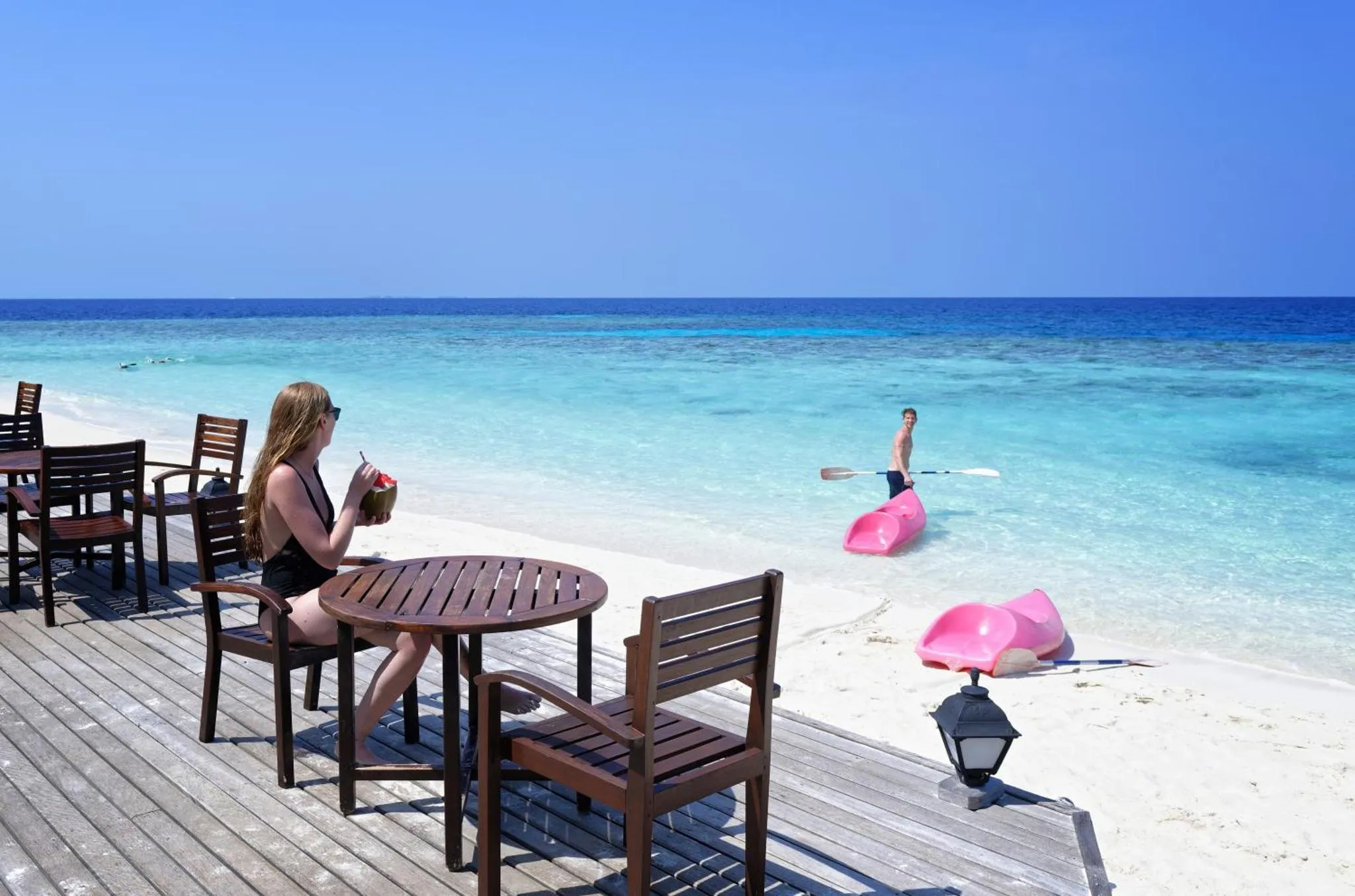 Une personne déguste une boisson à une table en bois sur une terrasse face à la mer.