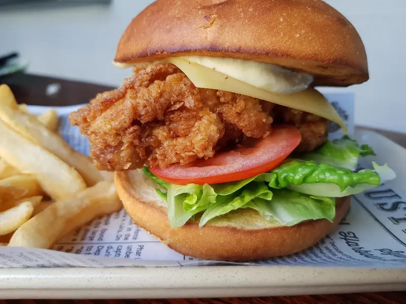 Un hamburger garni de poulet frit, de tomate et de laitue est servi avec des frites.