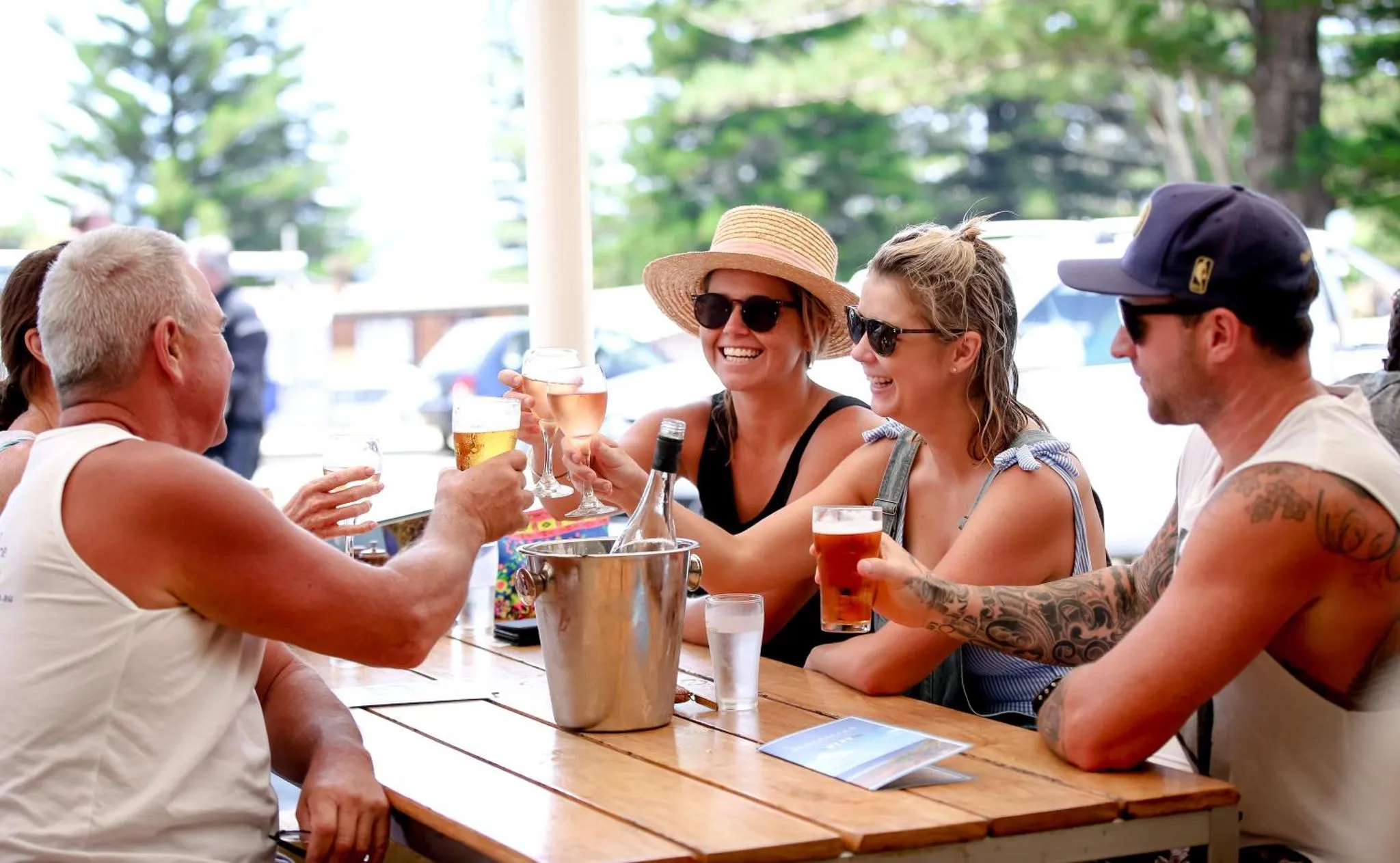 Des convives partagent des boissons autour d'une table ensoleillée.