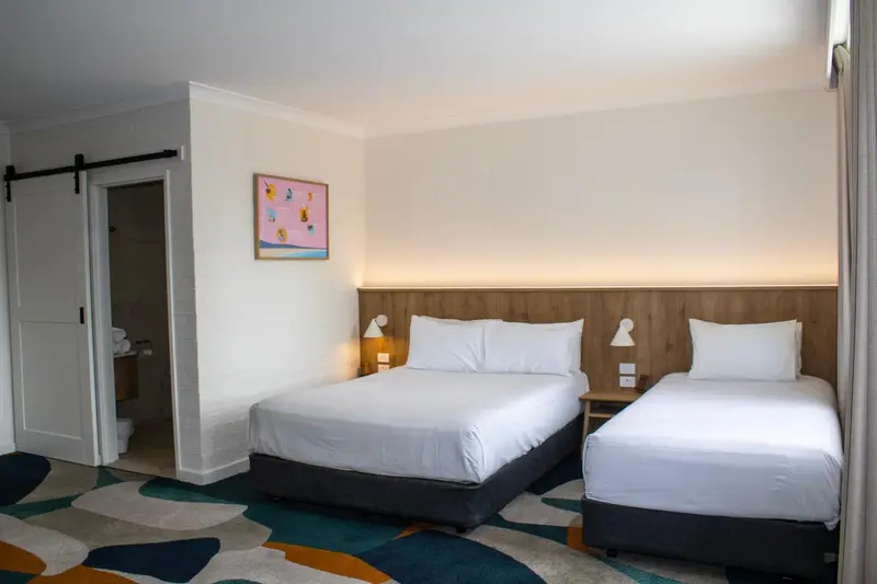 Une chambre lumineuse avec deux lits et une salle de bain visible.