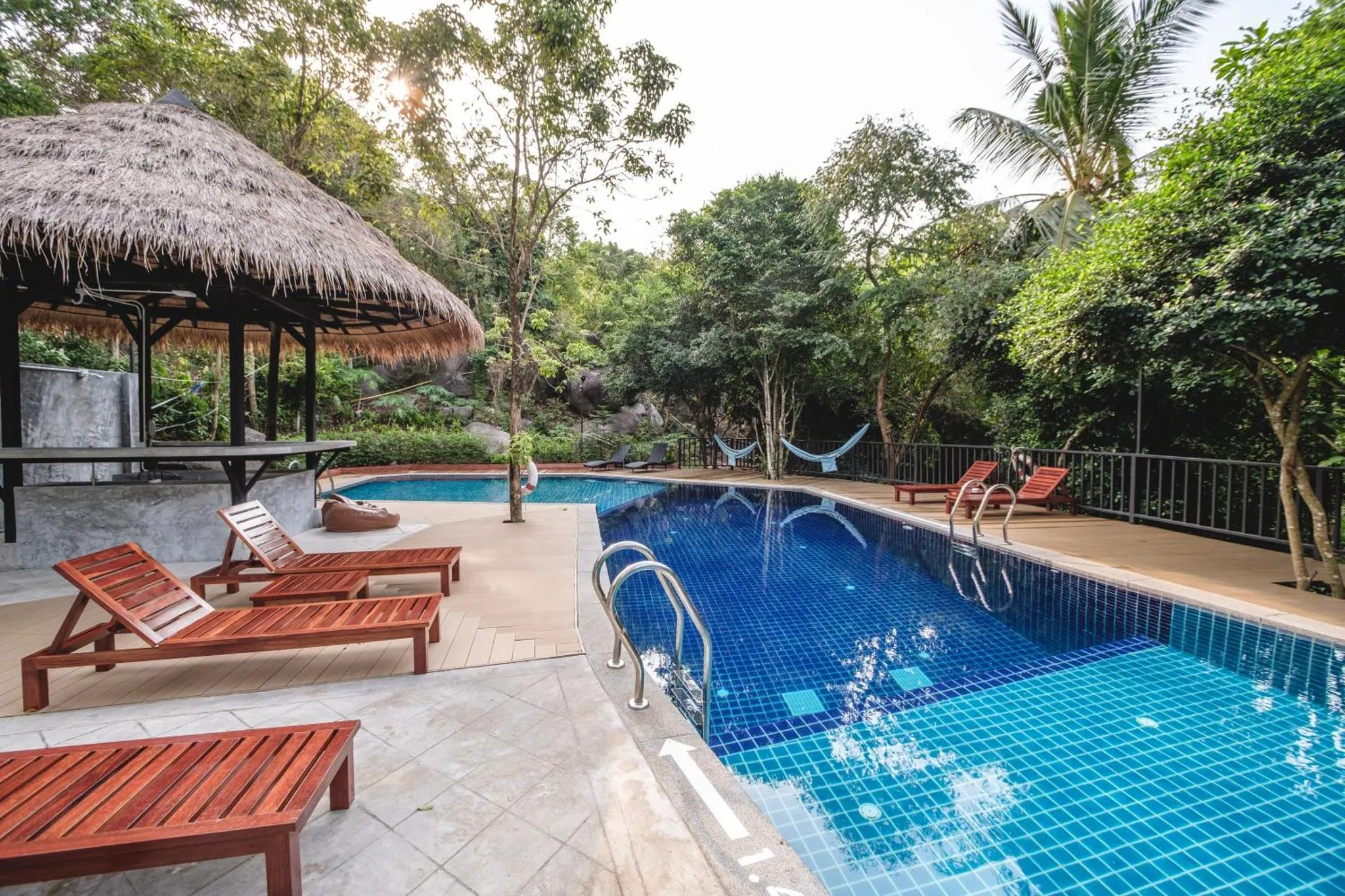Transats et parasols bordent une piscine turquoise dans un cadre tropical.