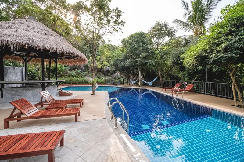 Transats et parasols bordent une piscine turquoise dans un cadre tropical.