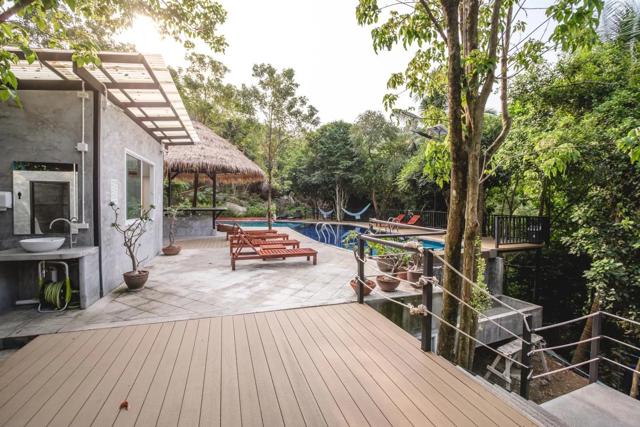 Terrasse en bois avec transats et piscine au milieu de la végétation.