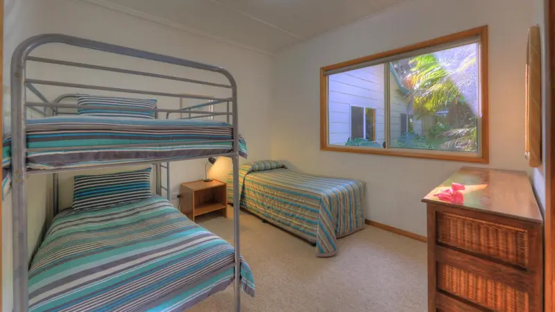 Une chambre avec des lits superposés et un lit simple près d'une fenêtre.