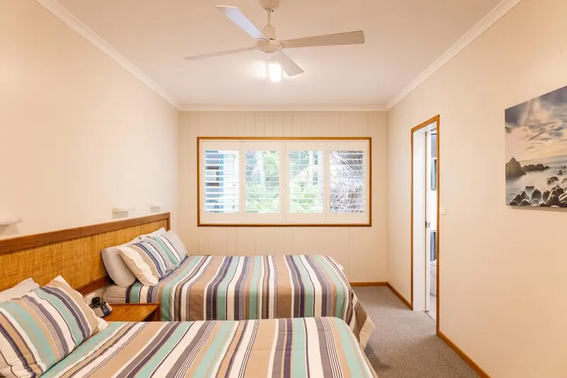 Chambre lumineuse avec deux lits simples et une fenêtre.