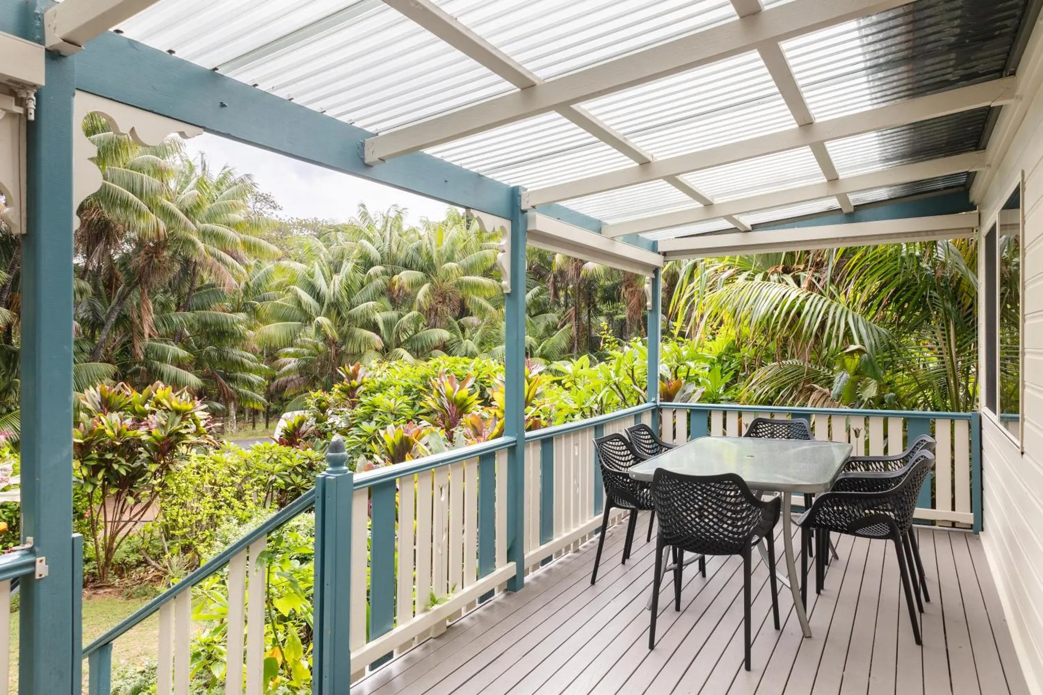 Terrasse en bois avec mobilier de jardin et végétation luxuriante en arrière-plan.