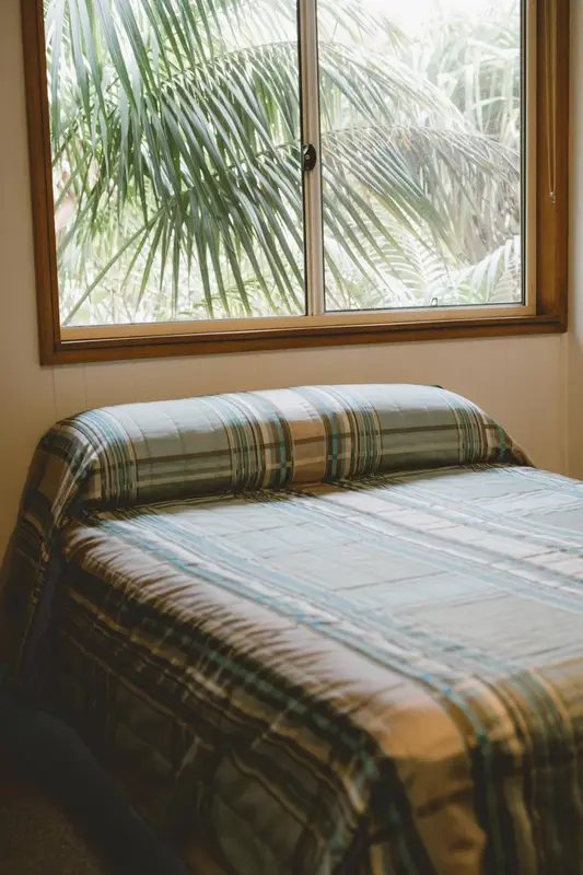 Un lit recouvert d'une couverture colorée est visible à travers une fenêtre.