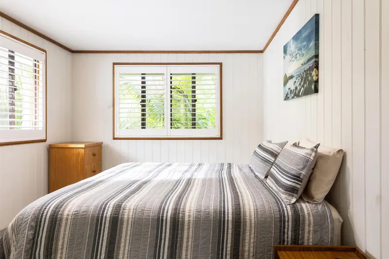 Une chambre lumineuse avec un lit fait et des stores aux fenêtres.