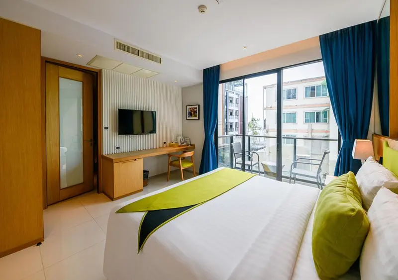 Une chambre lumineuse avec un lit recouvert d'une couverture verte et un bureau près d'une grande fenêtre.