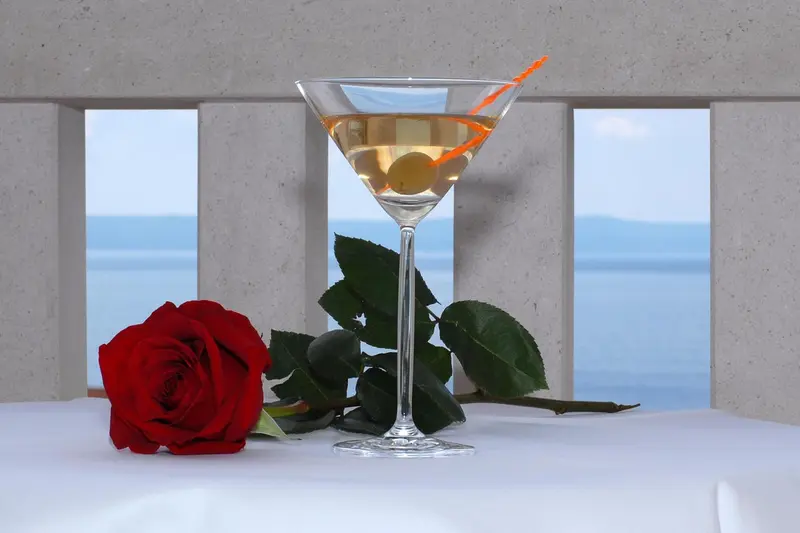 Un cocktail et une rose rouge sont posés sur une table blanche avec vue sur la mer.