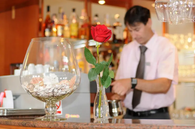 Un bar avec une rose rouge en décoration et un serveur en arrière-plan.