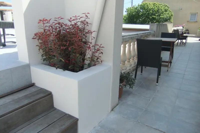 Terrasse carrelée avec mobilier de jardin et plantes en pot.