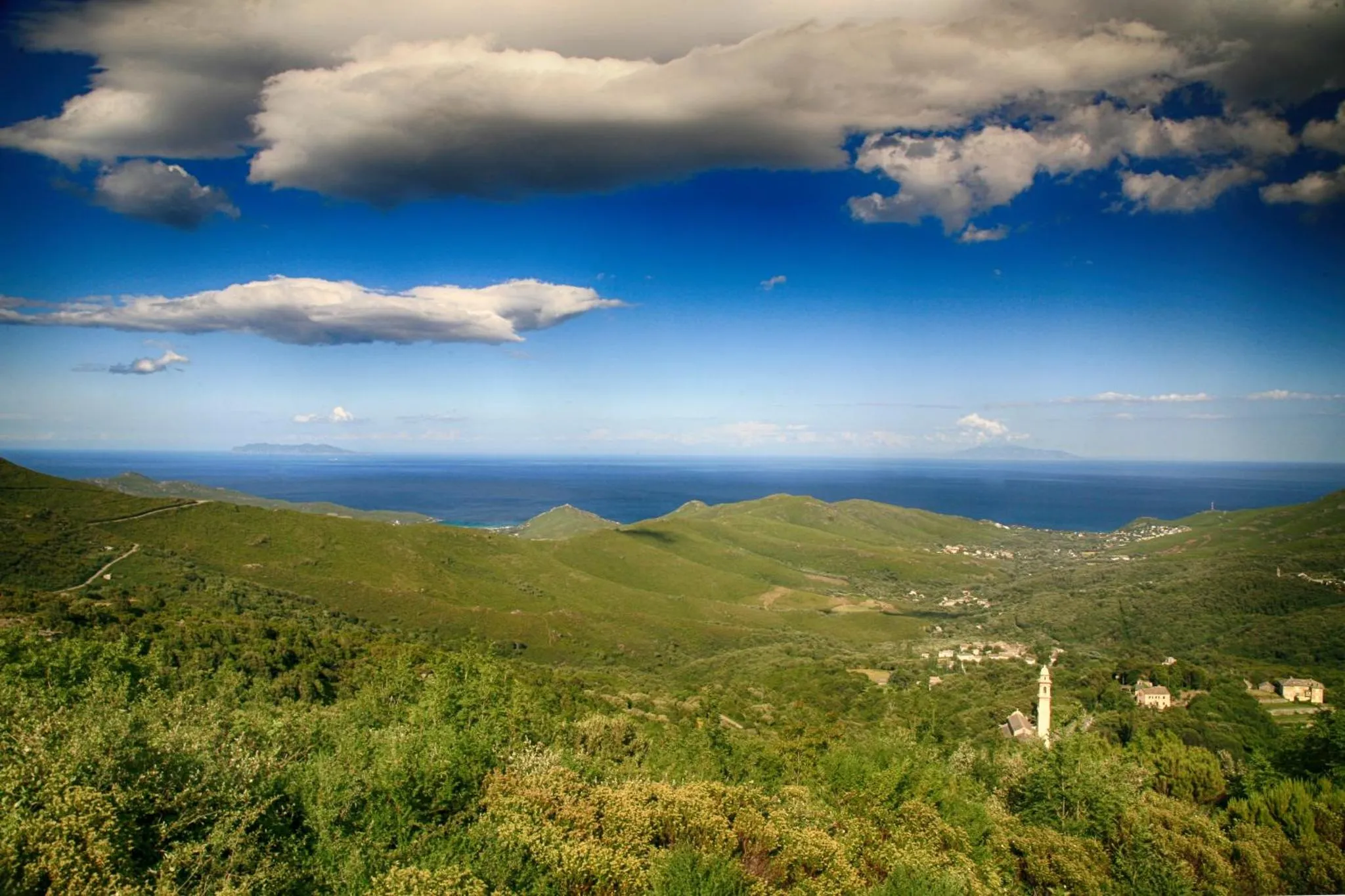 Paysage vallonné verdoyant surplombant la mer sous un ciel nuageux.