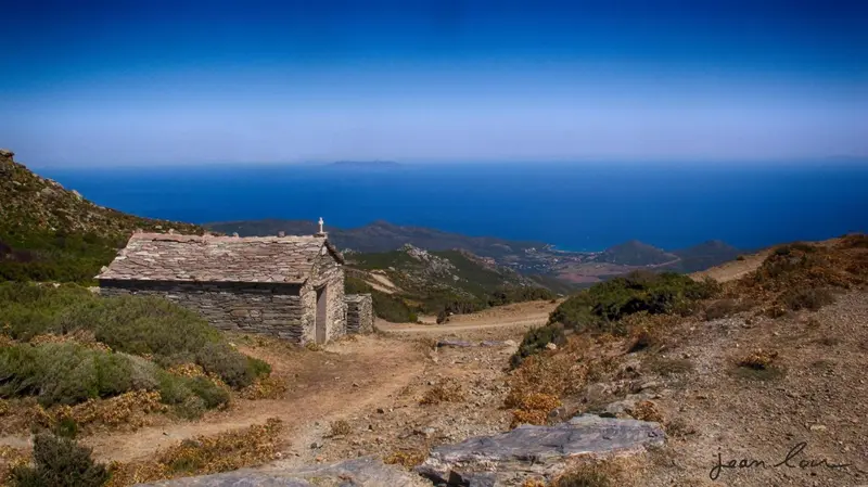 Petite chapelle en pierre sur une colline surplombant la mer et les montagnes.