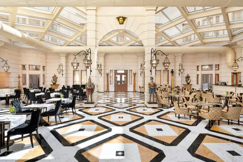 Vaste salle lumineuse avec un sol à motifs géométriques et des tables de restaurant disposées en rangées.