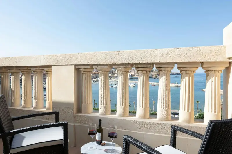 Vue d'une terrasse avec des fauteuils et une table basse, donnant sur un port de plaisance et la mer.