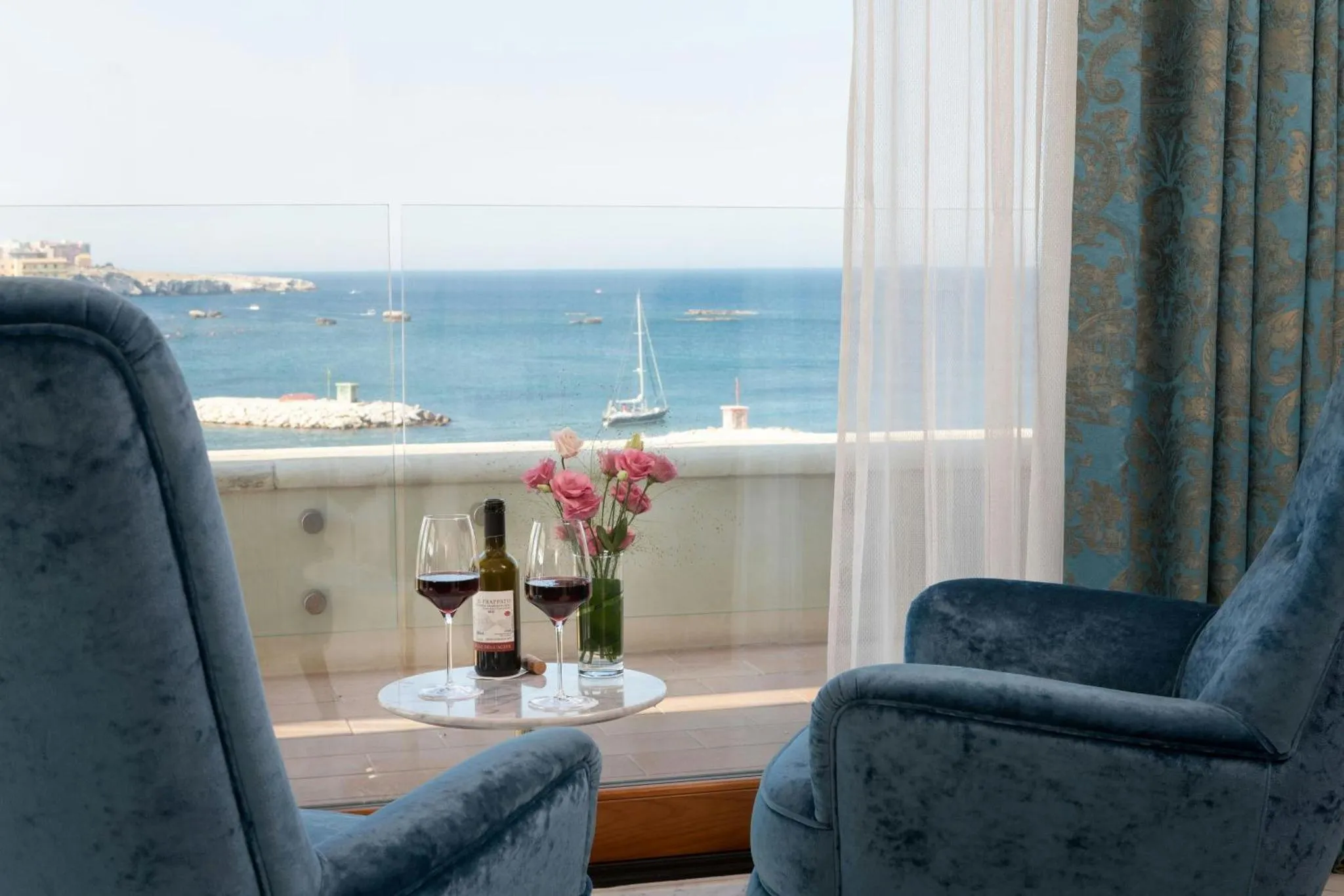 Deux fauteuils bleus et une table avec des verres de vin offrent une vue sur la mer.