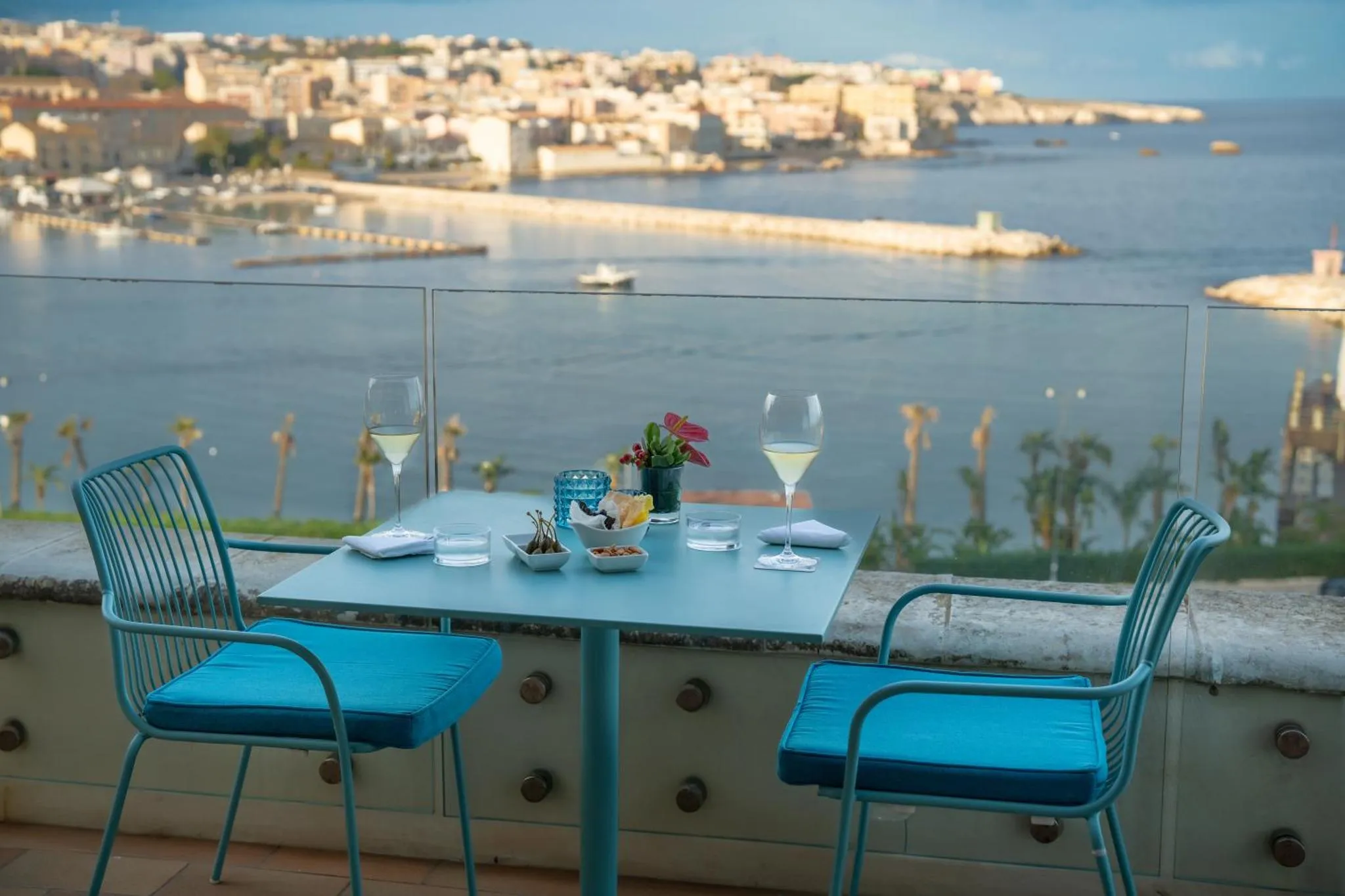 Une table est dressée sur une terrasse avec vue sur la mer et la ville.
