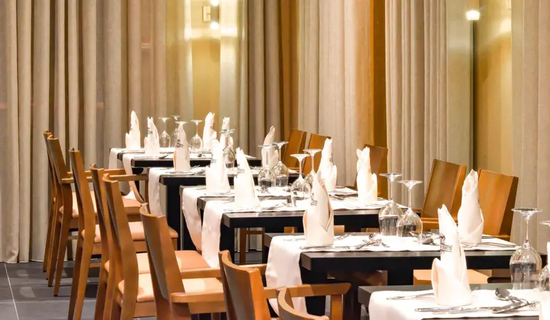 Tables dressées dans une salle de restaurant élégante avec des rideaux beiges.