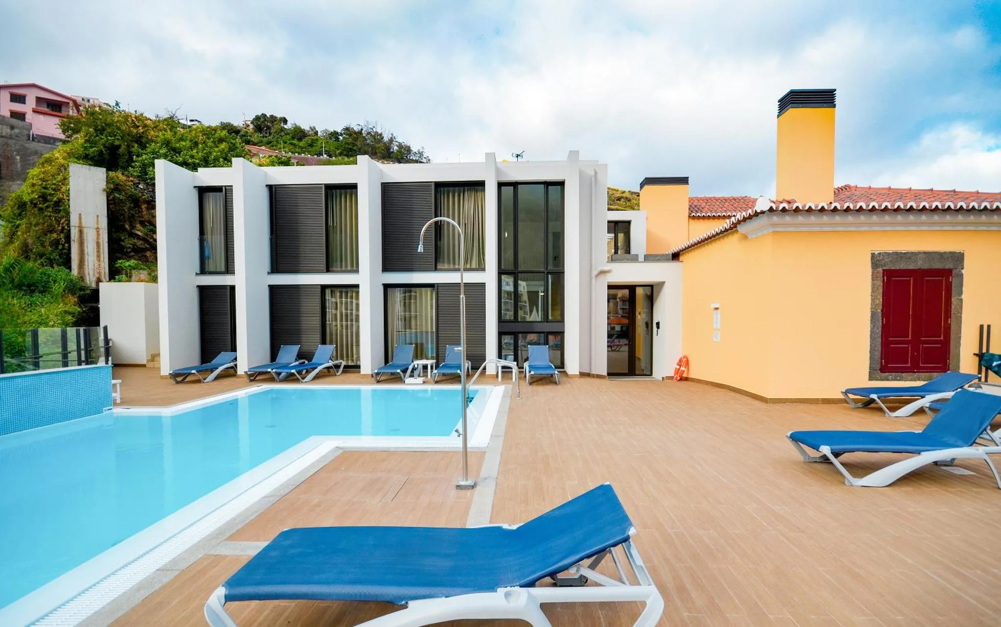 Transats bleus alignés au bord d'une piscine ensoleillée devant un bâtiment blanc.